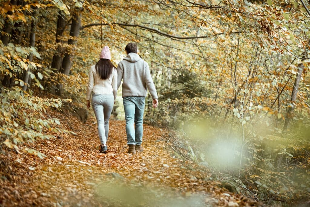 Paar spaziert durch einen herbstlichen Waldweg mit buntem Laub.