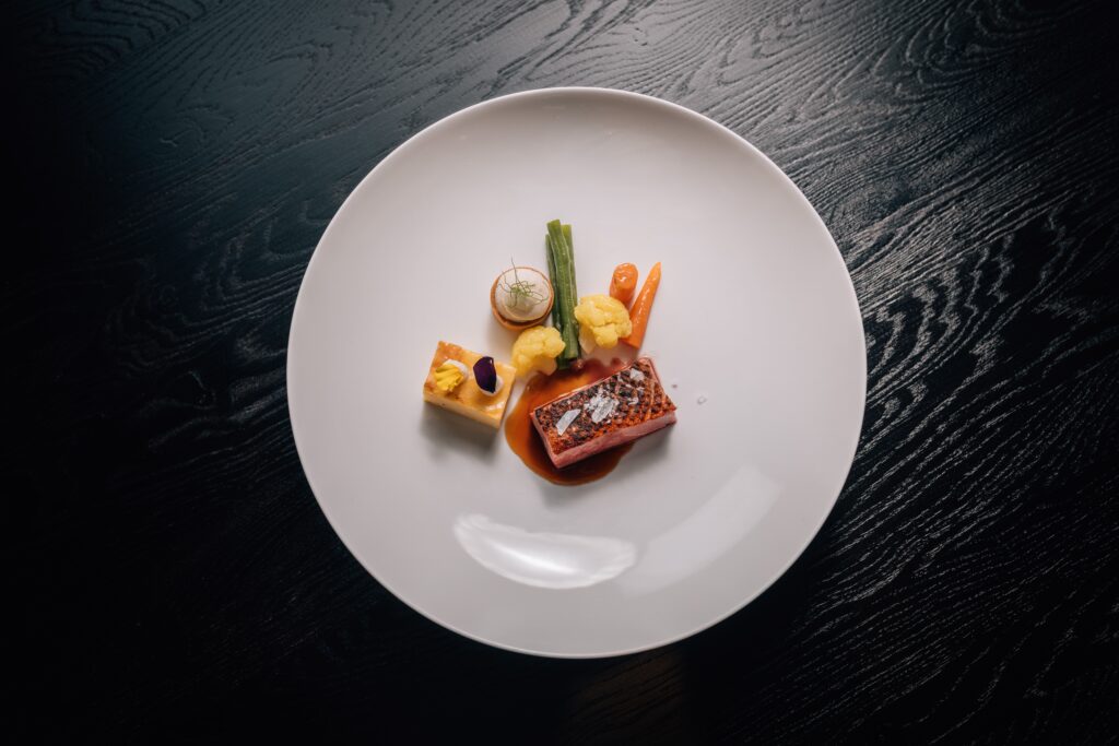 Gourmetgericht mit Gemüse und Sauce auf weißem Teller